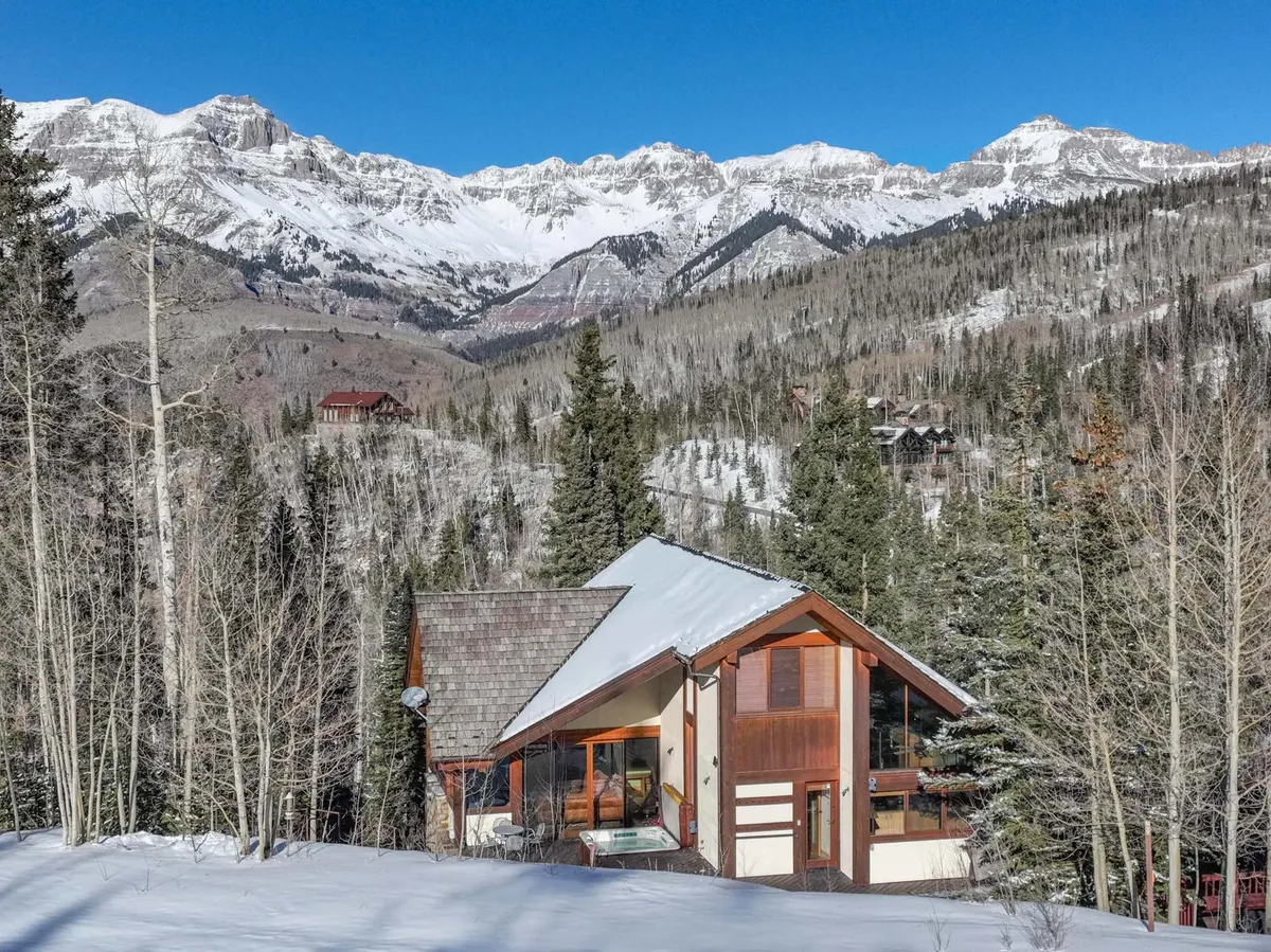 A panoramic view of the San Sophia mountain range behind a modern home, blanketed in snow. The expansive landscape and the home's large windows highlight the seamless connection between contemporary architecture and the inspiring natural vistas.