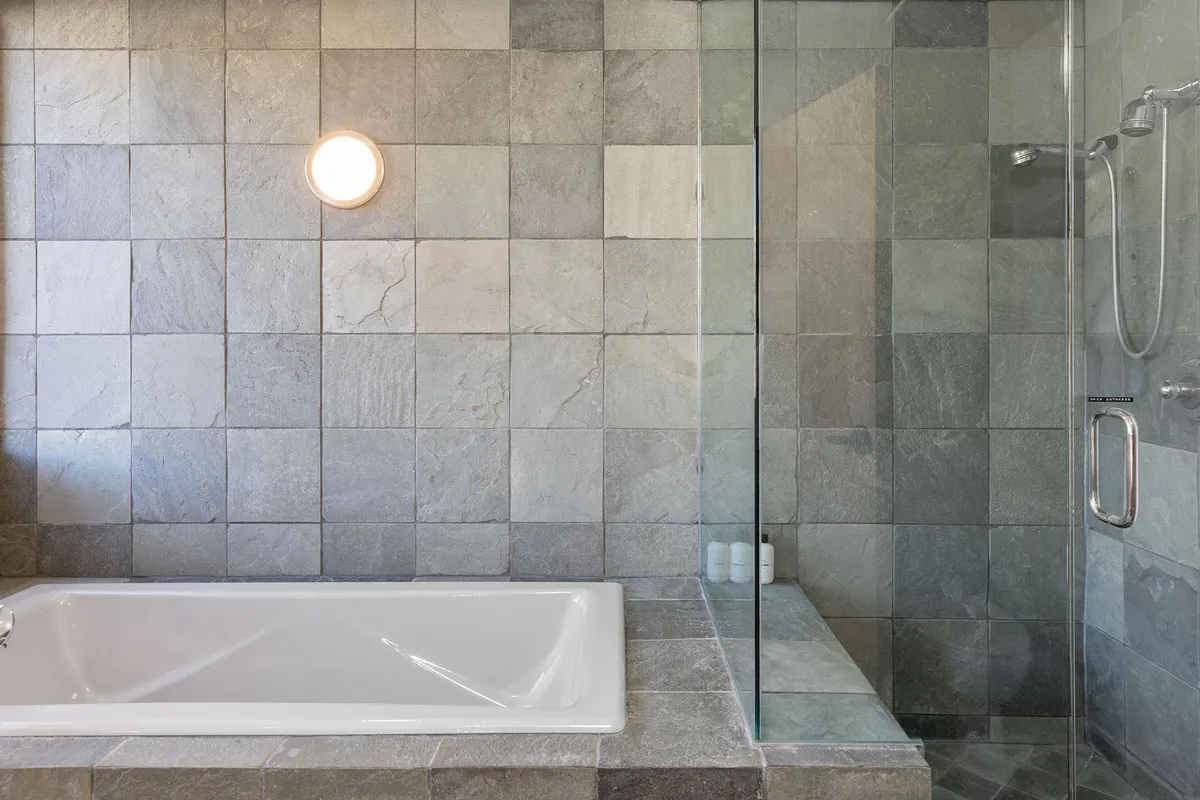 A spa-inspired bathroom featuring a soaking tub, a glass-enclosed steam shower, and slate tiles. Soft lighting and a modern design create a calming ambiance ideal for self-care and relaxation.