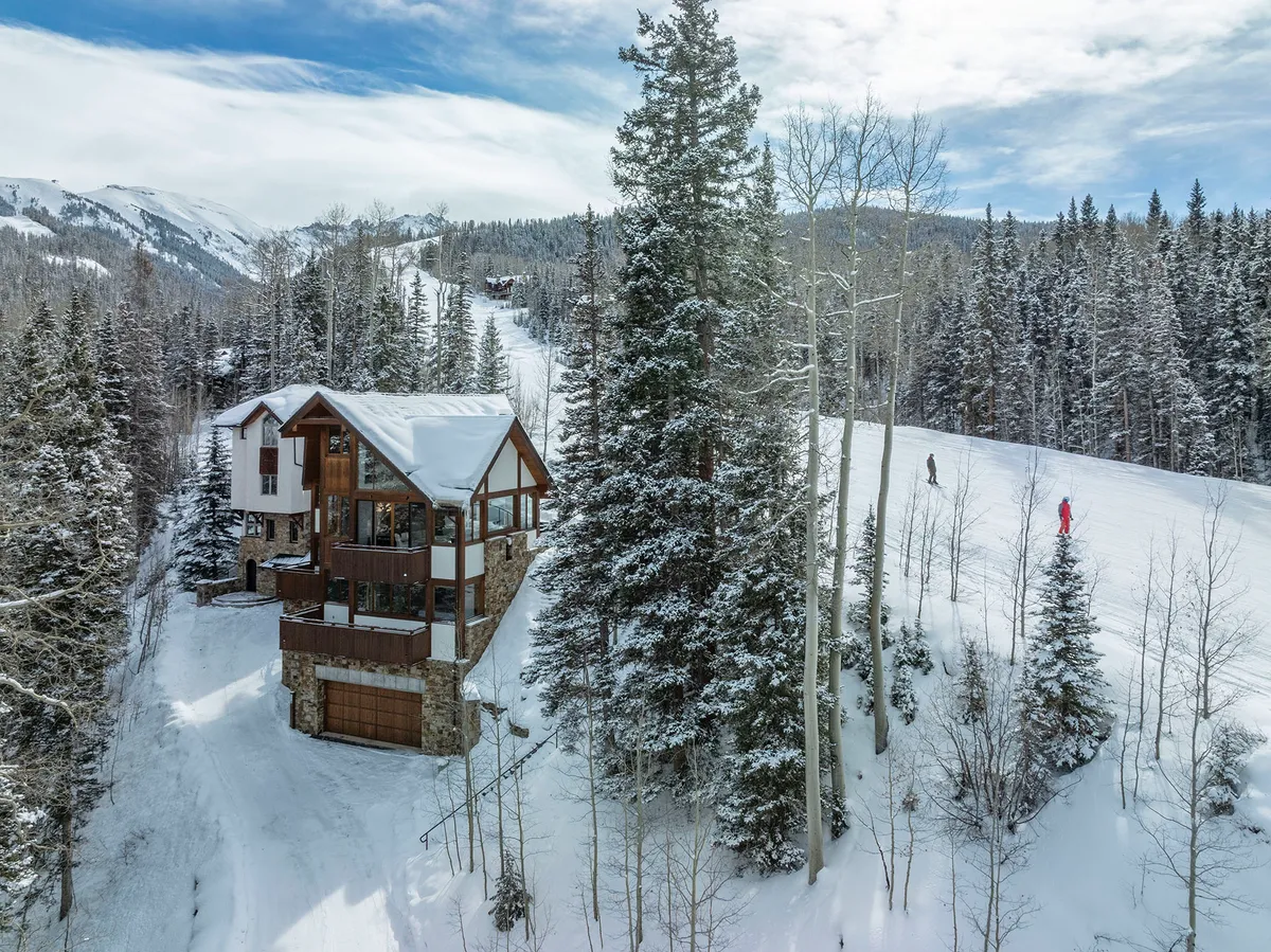 An expansive view of the chalet-style house surrounded by snowy landscape, with ski slopes and forested areas nearby. The image captures the excitement of mountain activities and the promise of après-ski relaxation within a cozy, private home.