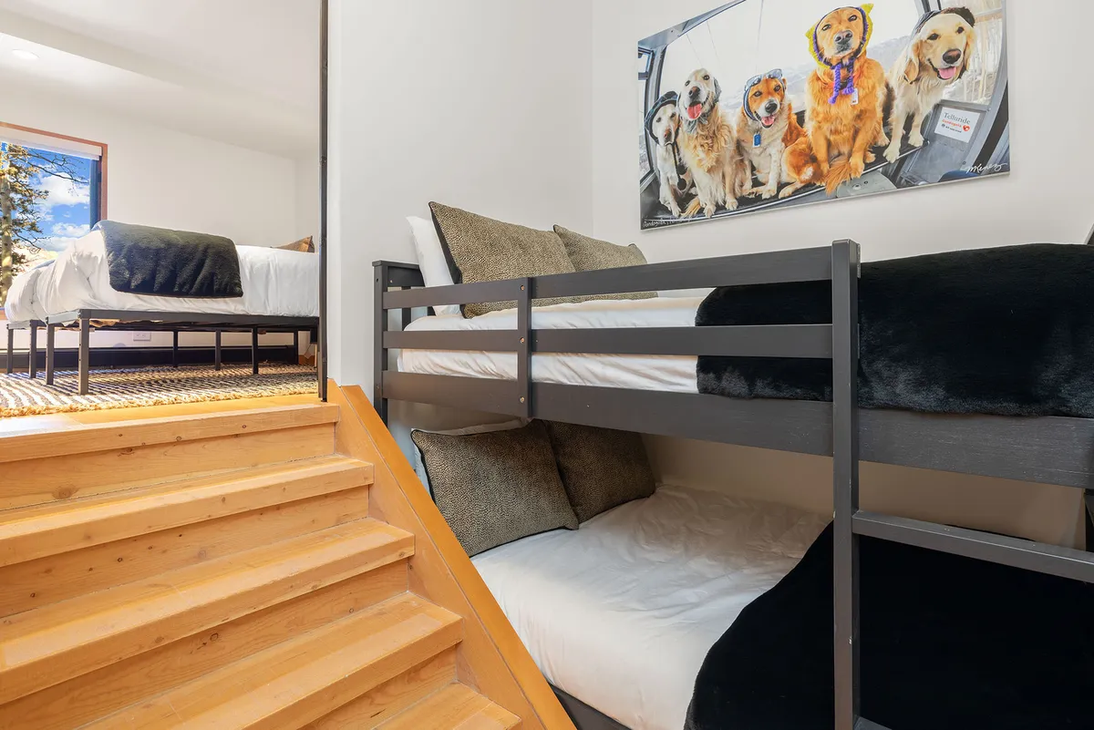 A cheerful, family-friendly bunk room with full-over-full bunk beds, playful dog-themed artwork, and a staircase leading up to the top bunks. The room is bright and inviting, designed for comfort and togetherness.