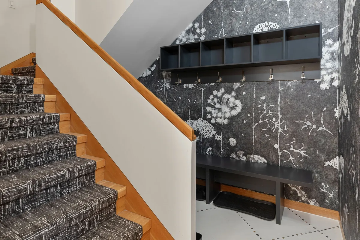 A practical mudroom with a bench, hooks for coats, and a decorative wall, situated near a staircase. The area is designed for storing shoes and gear, and for greeting guests upon entry.