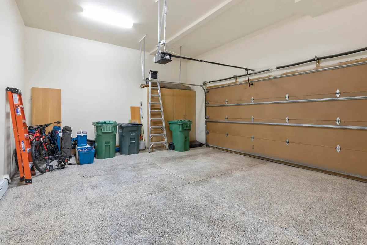 An interior view of the heated two-car garage, featuring organized storage areas, bicycles, garbage bins, a ladder, and ample space for vehicles and gear. The image conveys practicality and readiness for adventure.