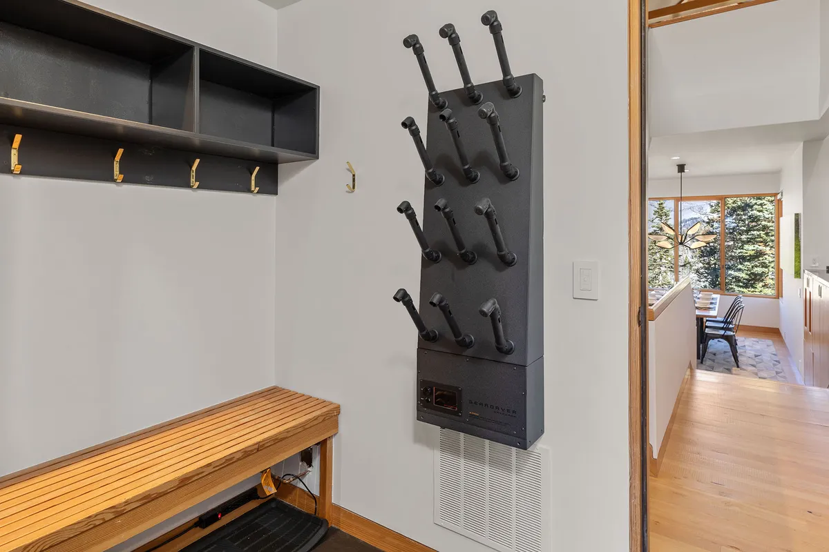 This image captures a functional ski room with a wall-mounted gear rack, a wooden bench, and shelves with hooks, designed for storing outdoor gear and preparing for alpine activities. The space looks inviting yet practical, echoing the luxury and convenience described in the section.