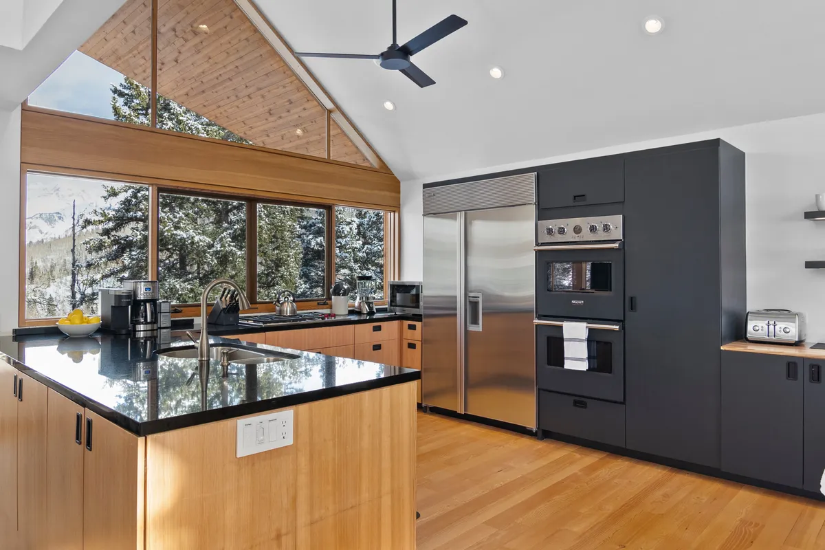 A sleek, modern kitchen featuring a central island, state-of-the-art stainless steel appliances, and expansive windows framing the surrounding mountains. The setup is ideal for entertaining and meal preparation, exemplifying the chef’s kitchen described in the text. Warm wood cabinetry adds a touch of mid-century flair.