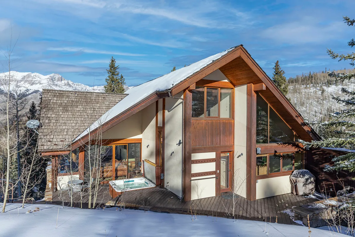 A tranquil exterior view showcasing large windows, a wooden deck, and a bubbling hot tub, all positioned to maximize enjoyment of the mountain scenery. The scene exudes relaxation, with the hot tub and deck inviting year-round use.