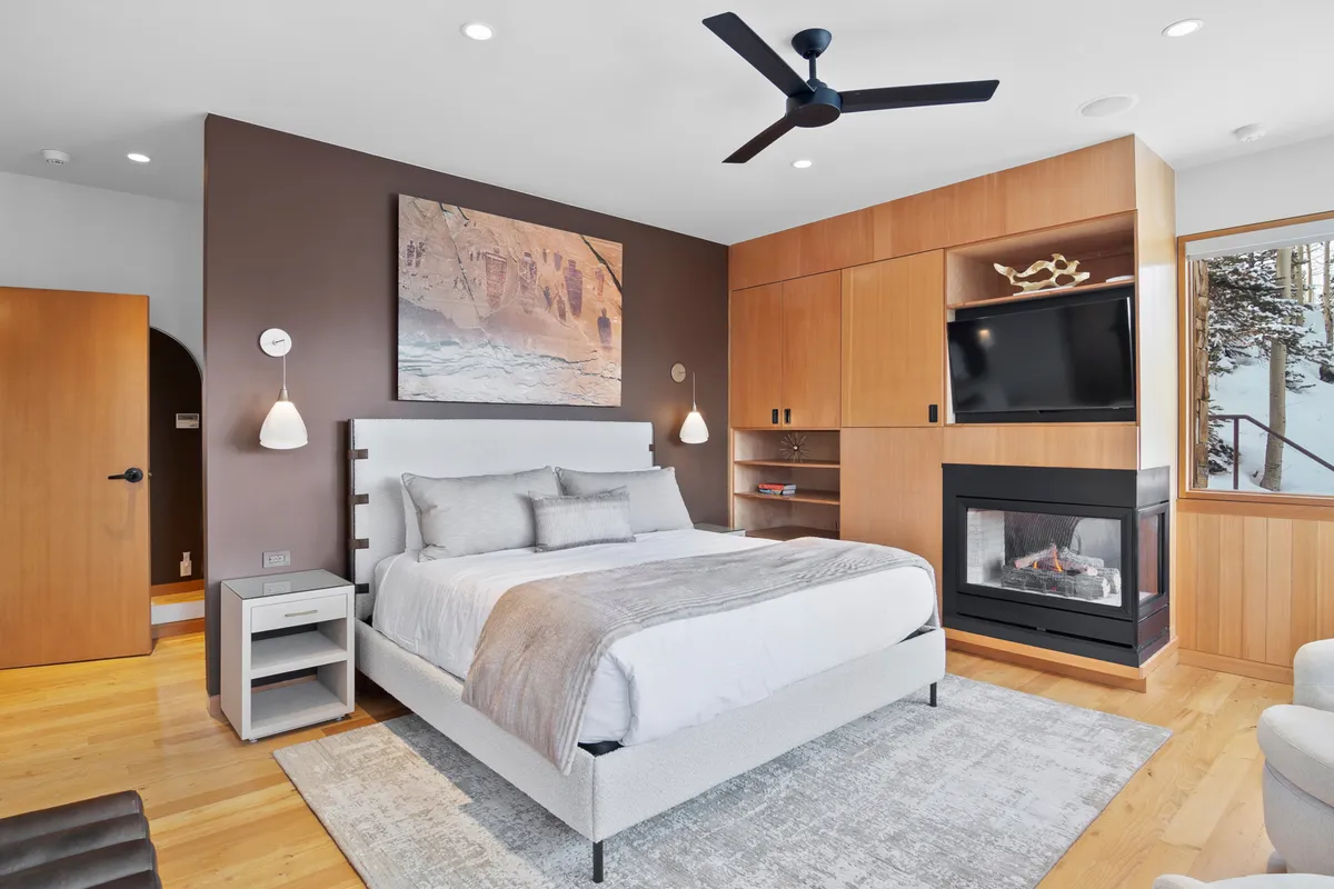 A king suite bedroom featuring a plush bed, a cozy gas fireplace, elegant wall art, and a large window offering serene views. The soft lighting and warm tones create an inviting atmosphere perfect for relaxation after a day of adventure.
