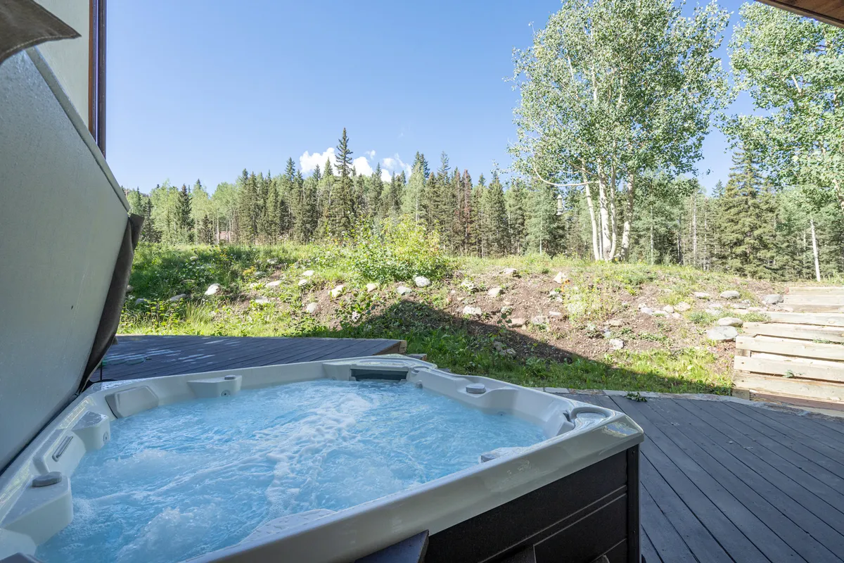 A tranquil outdoor hot tub surrounded by trees and under a clear sky. The scene evokes post-ski relaxation and offers a sense of privacy and connection to nature.